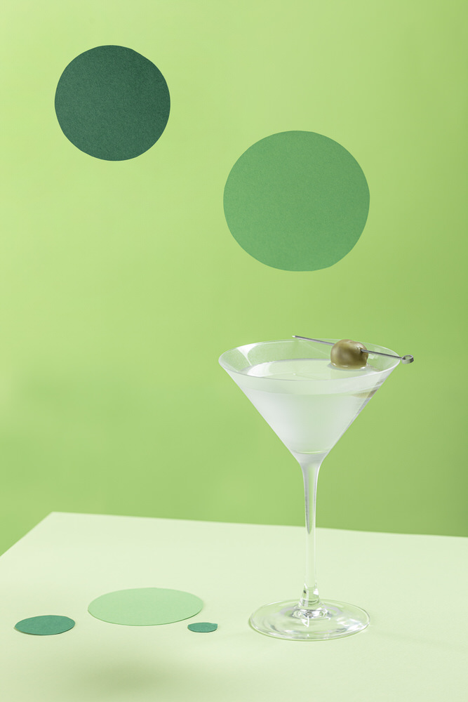 Martini con oliva in coppa su fondo verde con cerchi grafici, still life di beverage