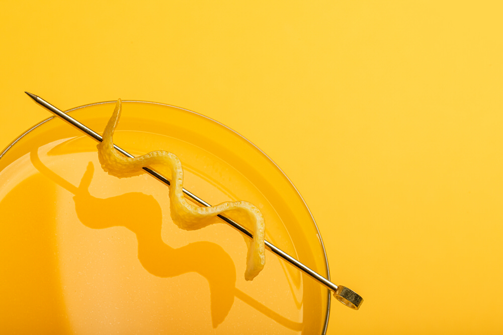 Dettaglio dall'alto di un cocktail con scorza di limone a spirale, fondo giallo pieno