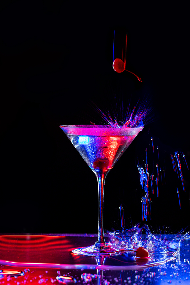 Cocktail in coppa martini in chiave scura con luci al neon e spruzzi d'acqua congelati