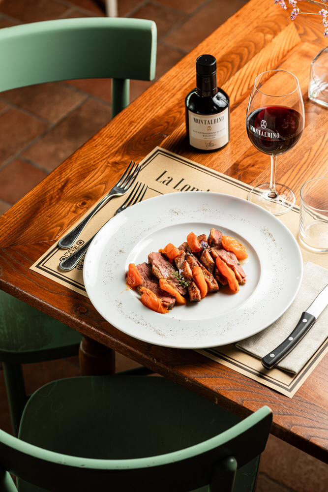 Piatto di carne con carote e vino rosso sul tavolo di un ristorante, luce naturale