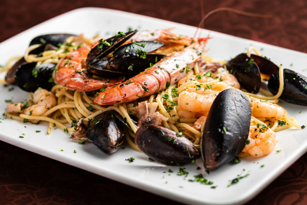 Spaghetti allo scoglio con gamberi, scampi e cozze su piatto rettangolare bianco