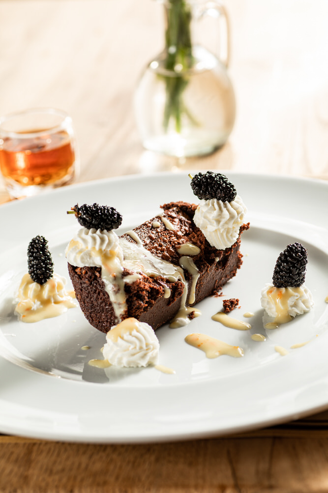Dolce al cioccolato con panna e more di gelso su piatto bianco, sfondo caldo sfocato