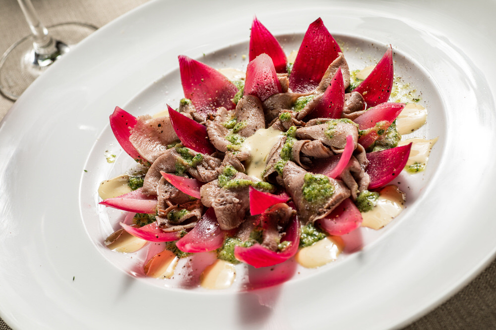 Piatto gourmet di carne affettata con petali di radicchio e salsa verde, impiattamento a fiore