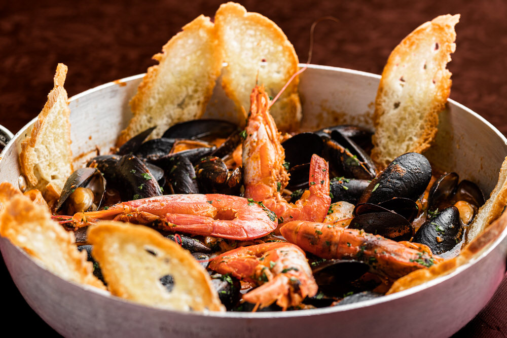 Zuppa di pesce con gamberi, cozze e crostini in casseruola su fondo scuro