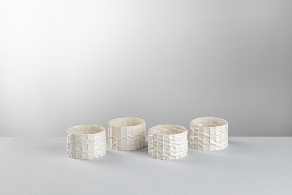 Quattro ciotole basse in ceramica bianca allineate, ognuna con una texture in rilievo diversa