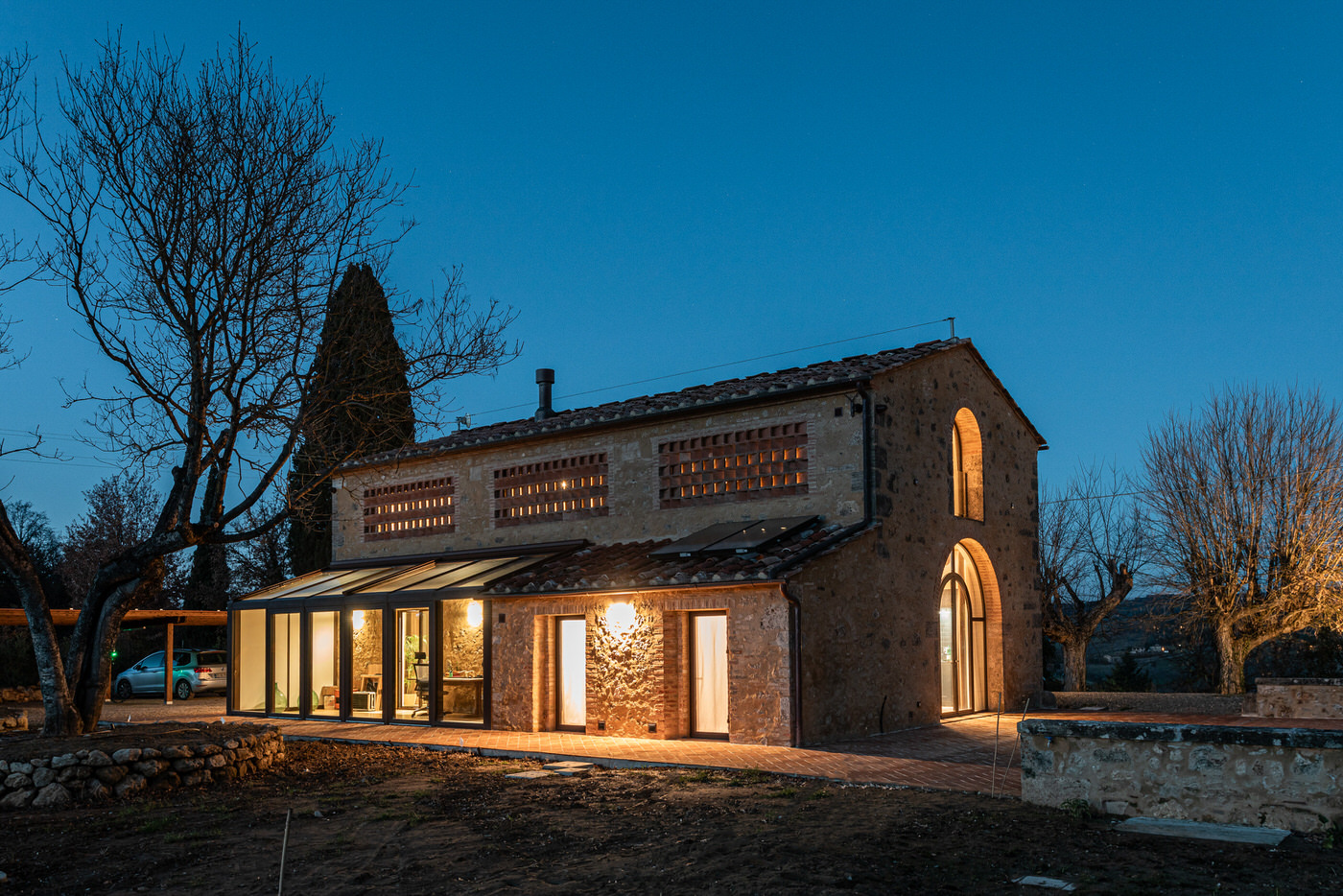 Casale storico in pietra all'ora blu, finestre illuminate e veranda vetrata moderna sul lato