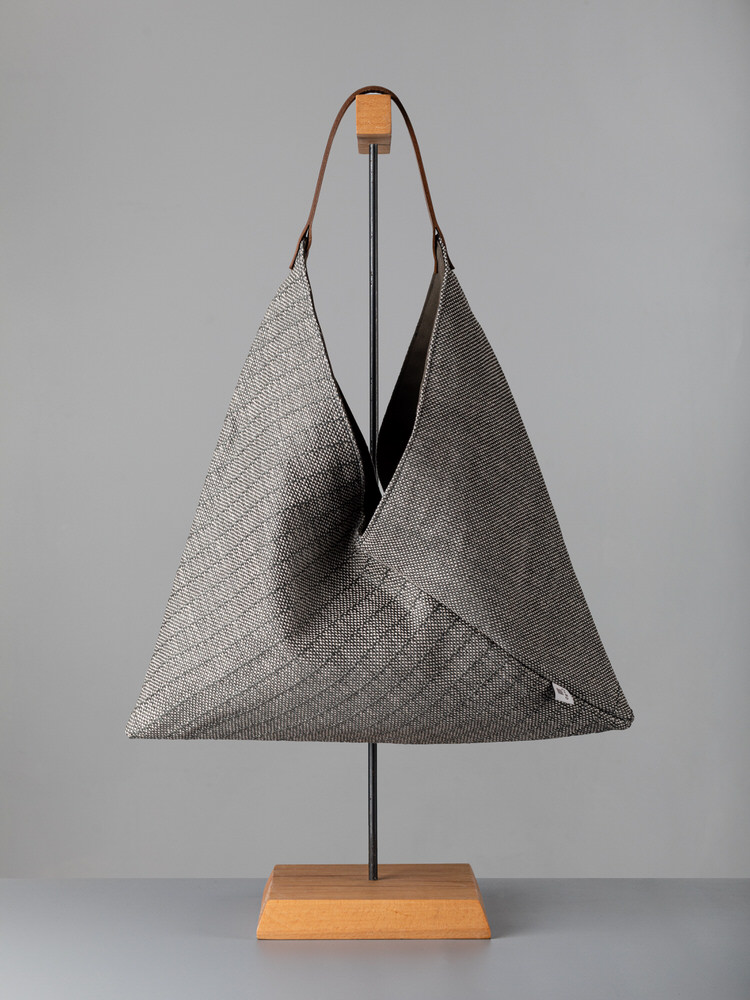 Borsa a tracolla in tessuto intrecciato grigio con manico in pelle, esposta su supporto in legno