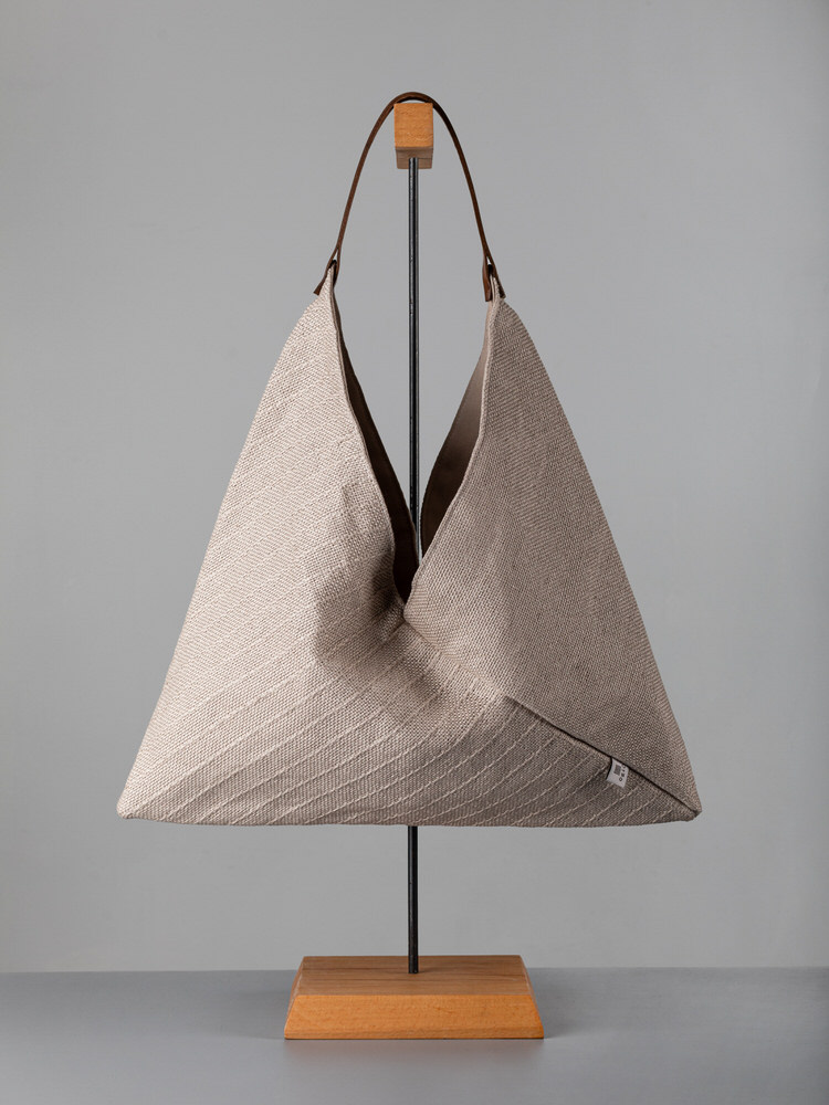 Borsa a tracolla triangolare in tessuto naturale beige su espositore in legno e metallo