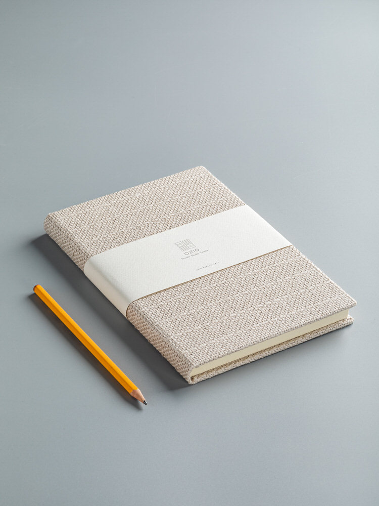 Taccuino con copertina in tessuto beige e fascetta di carta, accanto una matita
